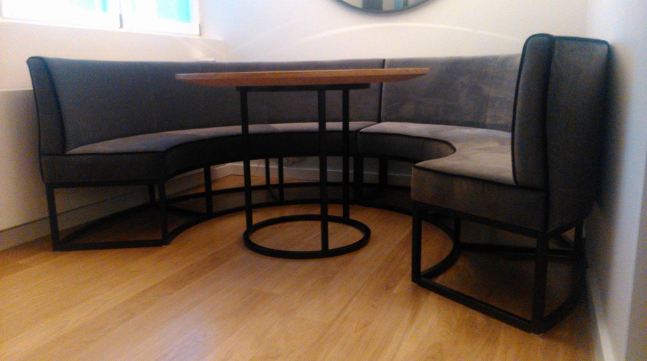 Tapicerowana, półokrągła ława z metalową konstrukcją i drewnianym blatem stołu, ustawiona na parkiecie.