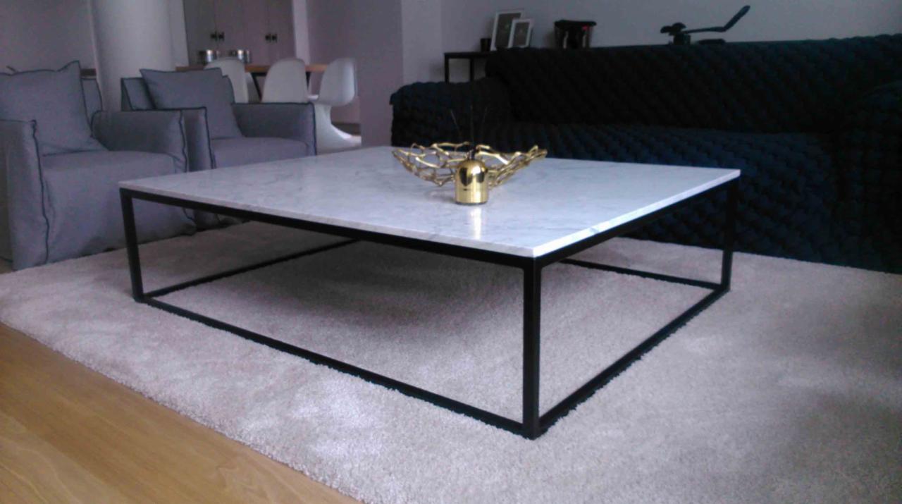 Stolik kawowy z marmurowym blatem i czarną metalową ramą, na puszystym dywanie, w tle szare fotele i ciemna sofa.