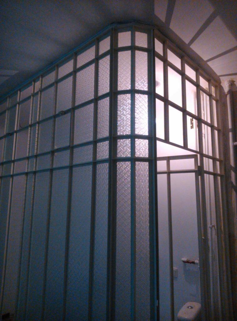 Szklana ścianka działowa z metalową ramą, wykonana na wymiar, oddzielająca przestrzeń w łazience, z widocznym fragmentem toalety.