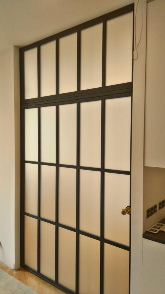 Nowoczesne drzwi wewnętrzne z czarną stalową ramą i matowym szkłem, złota klamka, widok z bliska.