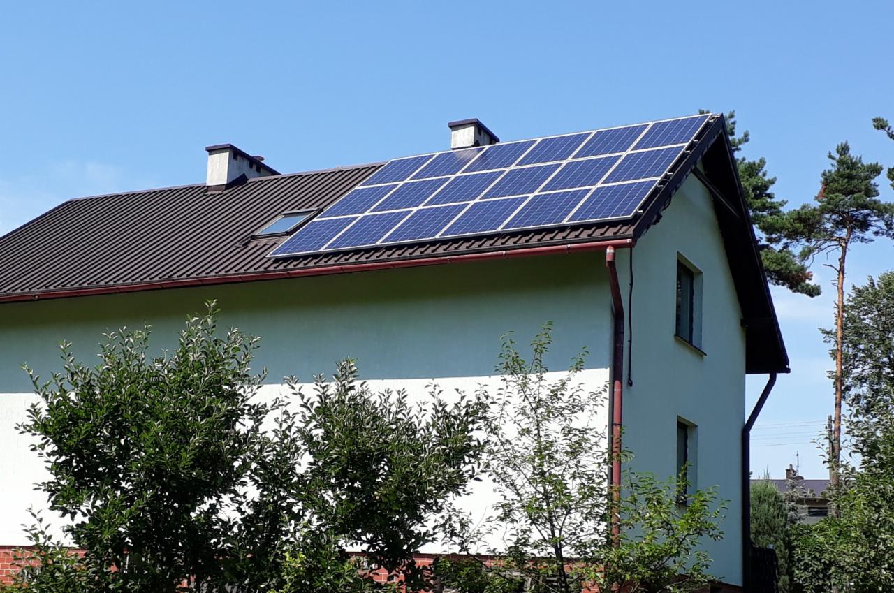 Dwuspadowy dach z brązową dachówką i panelami słonecznymi na jasnym domu jednorodzinnym, widok z poziomu ogrodu w słoneczny dzień.