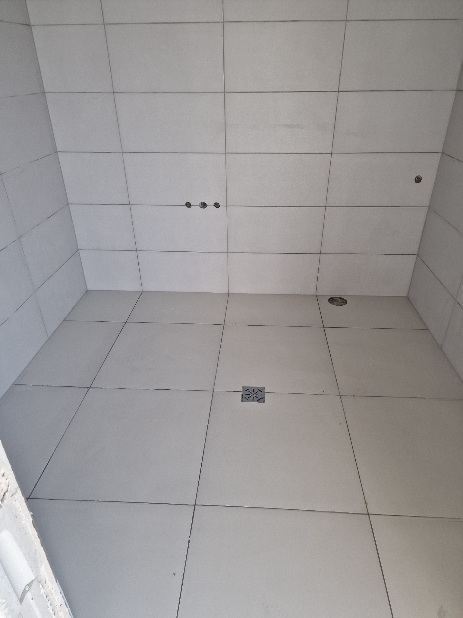 Wykończona łazienka w Końskich z jasnymi, kwadratowymi płytkami na ścianach i podłodze, widoczny odpływ liniowy i otwory pod armaturę.