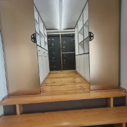 Nowoczesna garderoba z przesuwnymi drzwiami w odcieniach beżu, z drewnianą podłogą i schodami. Wnętrze szafy z białymi półkami i czarnym tłem.