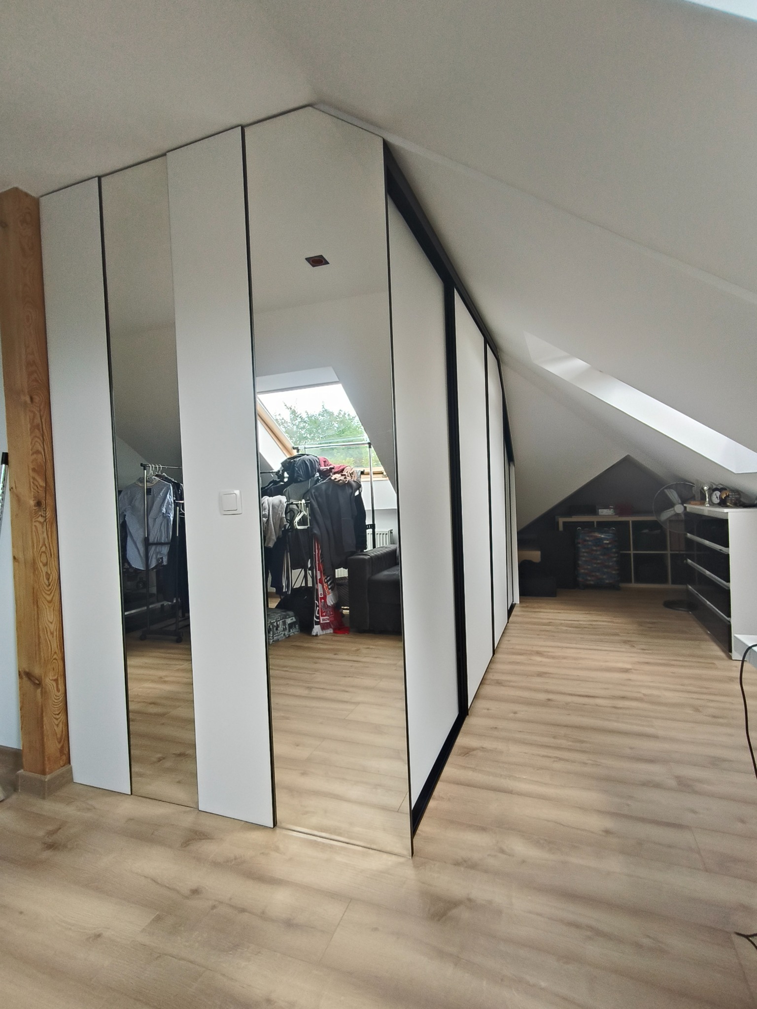 Szafa na wymiar z lustrzanymi frontami w pokoju na poddaszu. Widoczne skosy, drewniana podłoga i elementy garderoby odbijające się w lustrach.