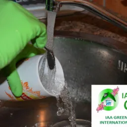 Osoba w zielonych rękawicach myje kubek pod bieżącą wodą w zlewie; widoczne logo firmy sprzątającej.