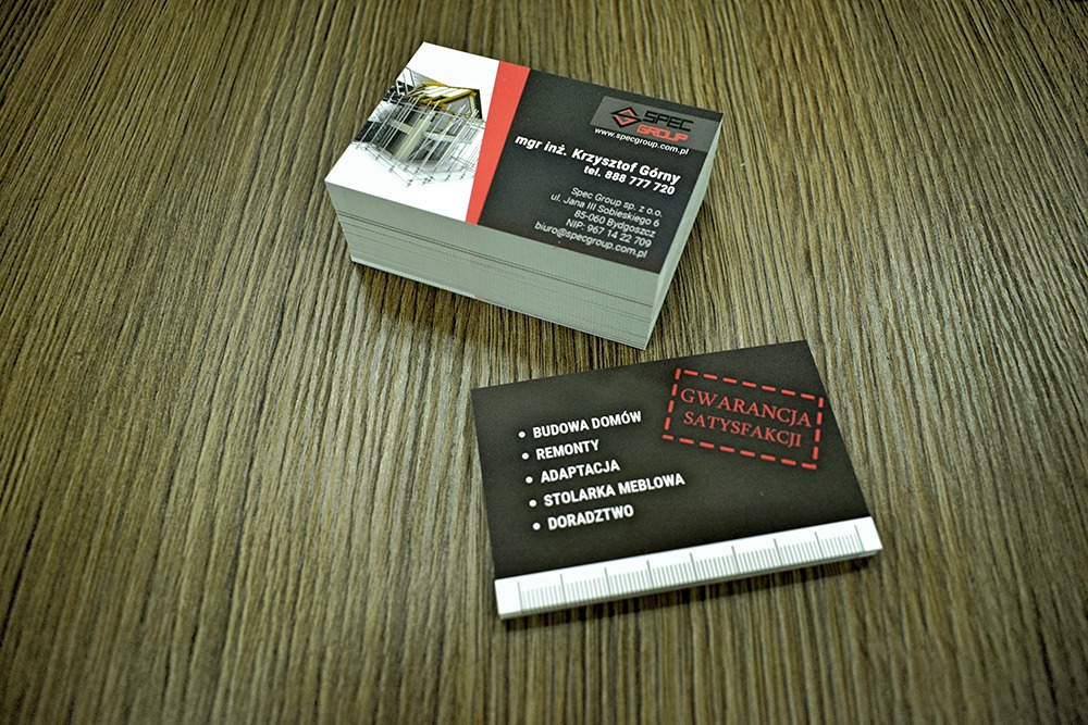 Stos wizytówek firmy budowlanej Spec Group z danymi kontaktowymi mgr inż. Krzysztofa Górnego, obok leży wizytówka z informacją o budowie domów, remontach, adaptacjach, stolarce meblowej...