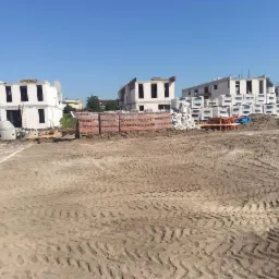 Plac budowy z widocznymi fundamentami domów w stanie surowym otwartym, ułożone materiały budowlane, ślady opon na ziemi.