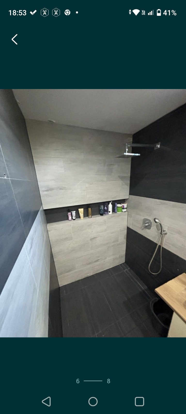 Nowoczesna kabina prysznicowa z szarymi płytkami imitującymi drewno, wnęka na kosmetyki z oświetleniem punktowym i czarnymi akcentami na ścianach.