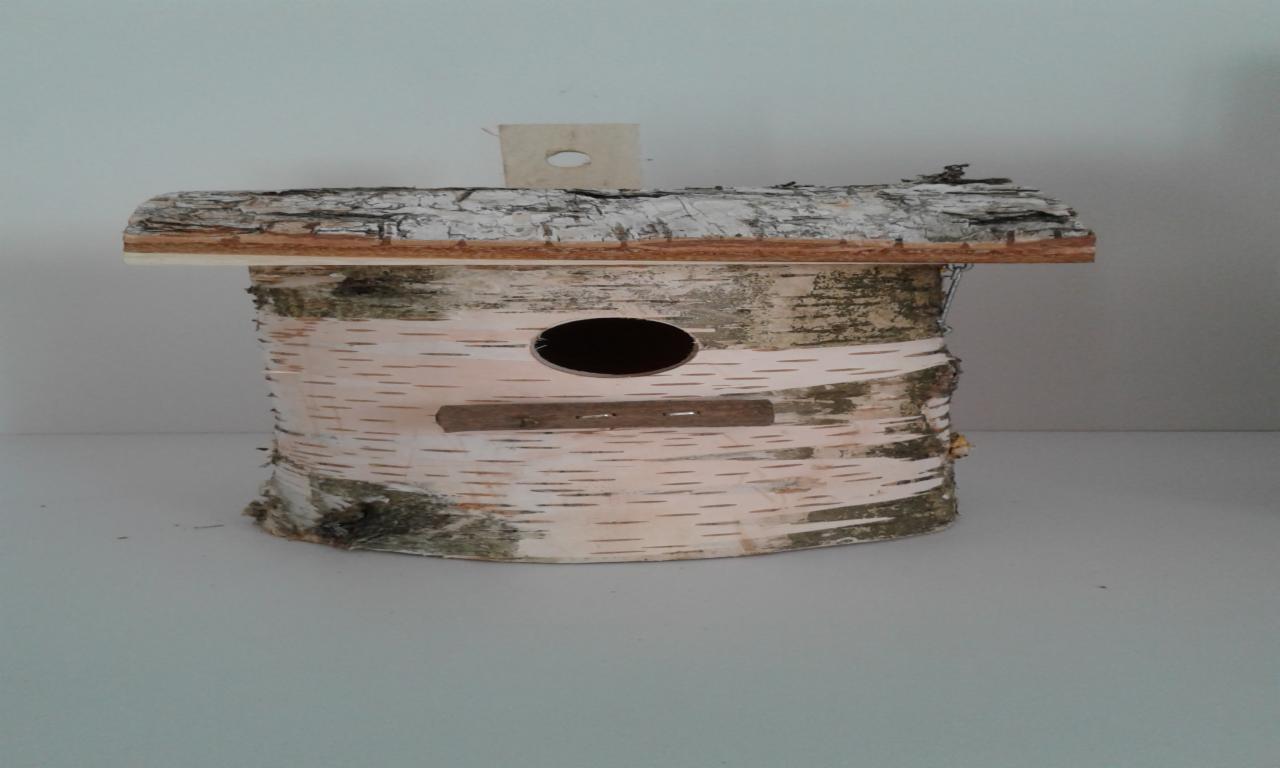 Drewniany domek dla ptaków wykonany z kory brzozowej, z okrągłym otworem wejściowym i daszkiem z kory.