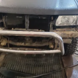 Przód samochodu terenowego z zamontowanym chromowanym bull barem, widoczny w warsztacie podczas prac montażowych.