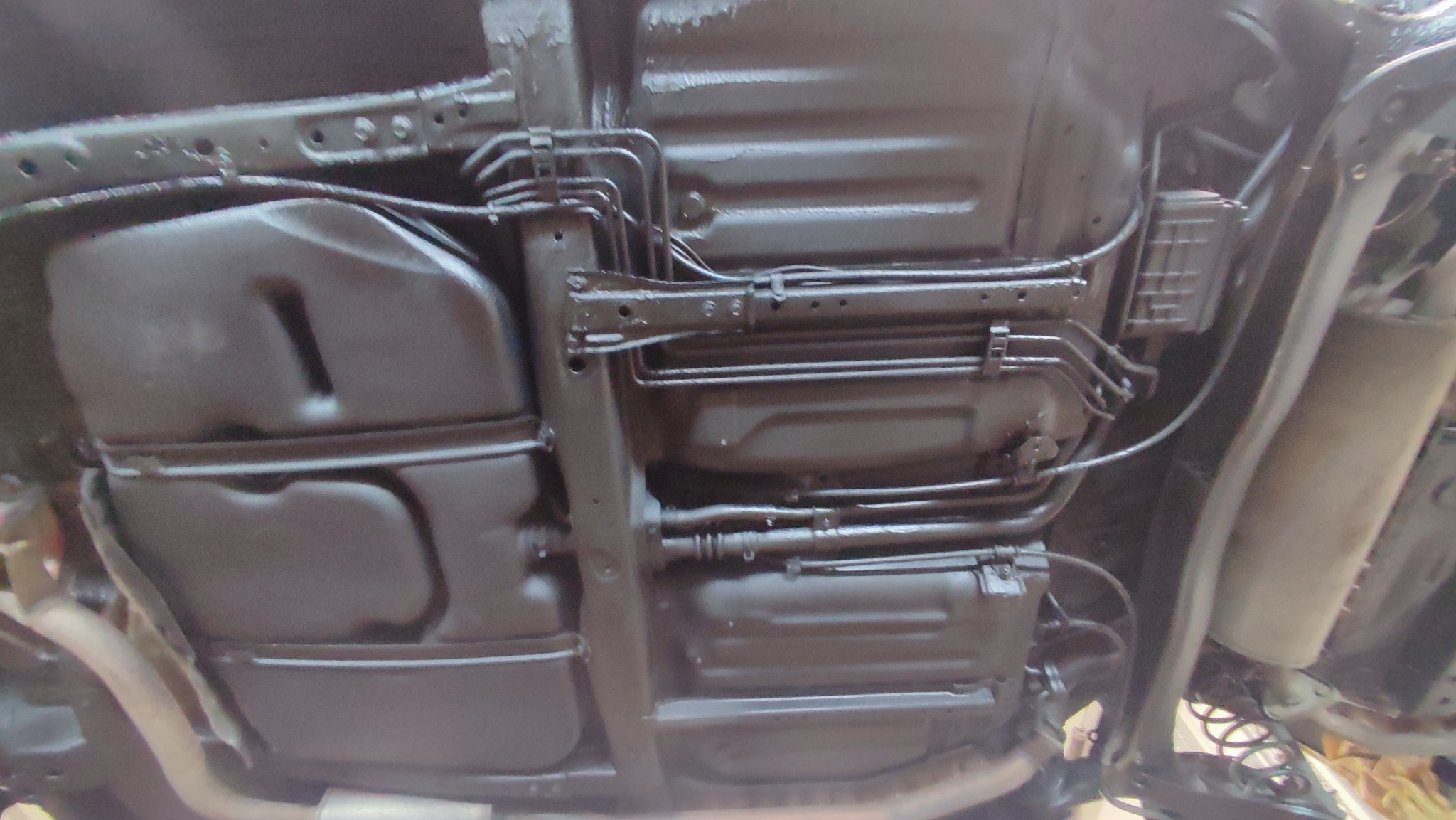 Podwozie samochodu po zabezpieczeniu antykorozyjnym, widoczne elementy zawieszenia, zbiorniki i przewody pokryte jednolitą, czarną powłoką ochronną.