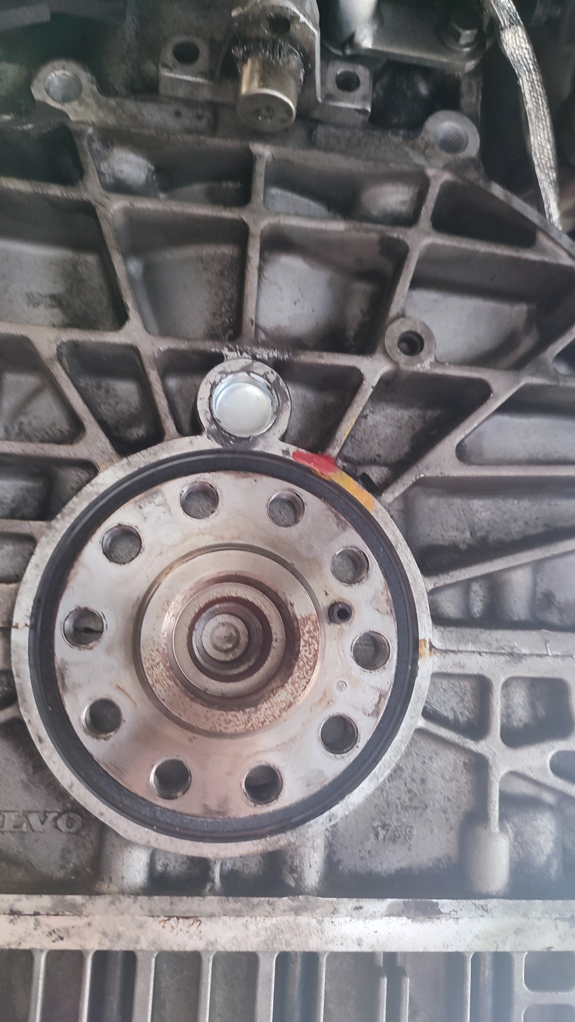 Widok z bliska na fragment silnika samochodowego z widocznym kołem zamachowym i blokiem silnika, na którym widoczne są ślady użytkowania i zabrudzenia.