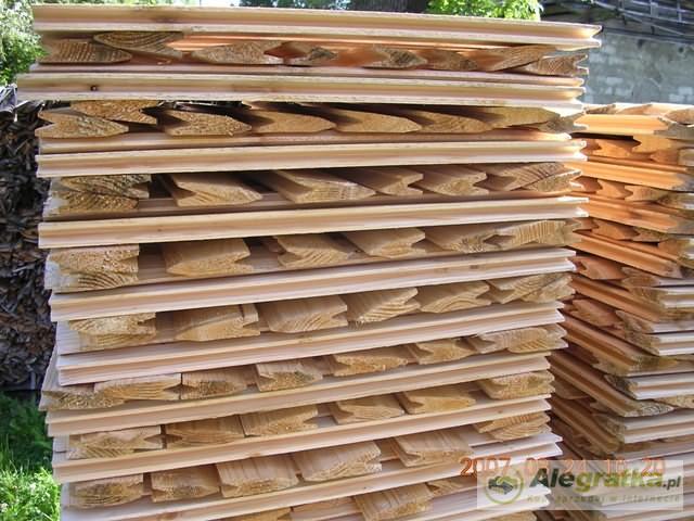 Stos ułożonych, surowych, drewnianych gontów z wyprofilowanymi krawędziami, przygotowanych do montażu na dachu.