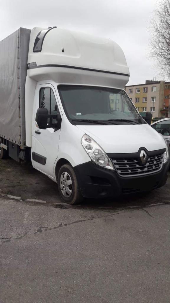 Biały samochód dostawczy Renault Master z plandeką i podwyższoną kabiną, zaparkowany na asfaltowym placu w pochmurny dzień.