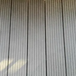 Szare deski kompozytowe tarasu ułożone równolegle, z widocznym delikatnym cieniowaniem od słońca.