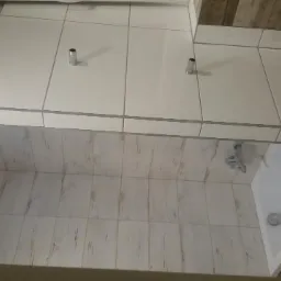 Wykończona łazienka z białymi płytkami na ścianach i podłodze, widoczna wanna, bateria i akcesoria łazienkowe, z dekoracyjnymi płytkami imitującymi drewno na jednej ze ścian.