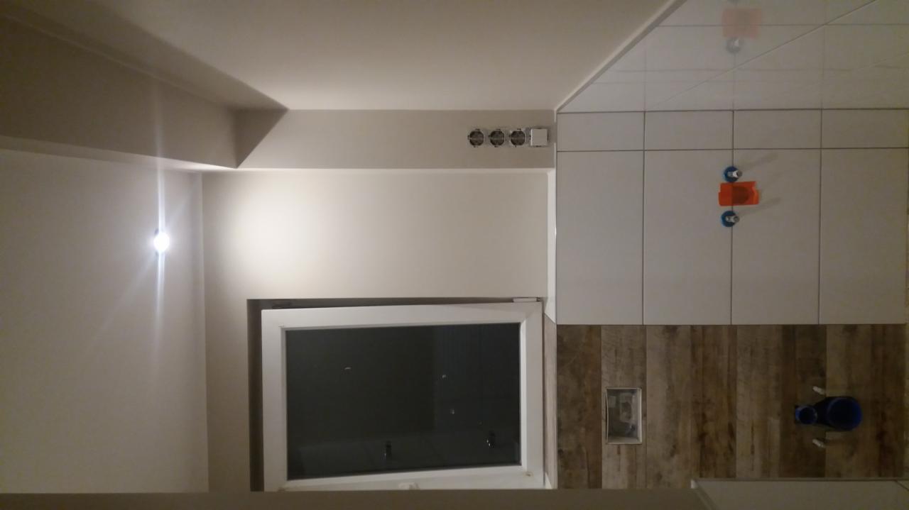 Łazienka w trakcie remontu: białe płytki ułożone na górze ściany z pomarańczowymi krzyżykami dystansowymi, dolna część ściany wykończona płytkami imitującymi drewno, widoczne otwory na gniazdka...