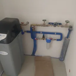 System uzdatniania wody AquaSoft z niebieskimi rurami i zaworami zamontowany w pomieszczeniu. Widoczne przyłącza i filtr.