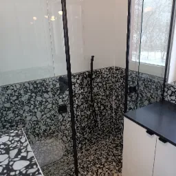 Nowoczesna kabina prysznicowa z czarnym osprzętem i wzorzystymi płytkami w stylu lastryko, widok na zimowy krajobraz za oknem.