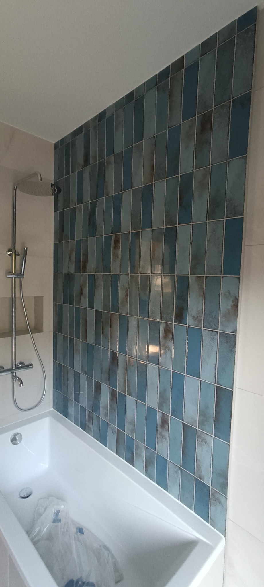 Nowoczesna łazienka z wanną i prysznicem deszczownicą, ściana wyłożona pionowymi, niebieskimi płytkami z efektem ombre.