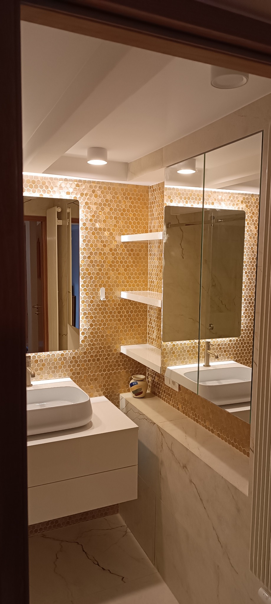 Nowoczesna łazienka z mozaiką w odcieniach złota, białymi półkami i umywalką nablatową, oświetlenie LED podkreśla fakturę płytek.