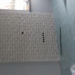 Fragment ściany wykończonej białą cegłą dekoracyjną, z widocznymi otworami na gniazdka elektryczne i instalację, zabezpieczone podłogi folią ochronną.