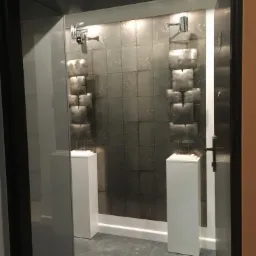 Nowoczesna łazienka z metalicznymi płytkami na ścianie, oświetleniem punktowym i dekoracyjnymi rzeźbami na białych postumentach.