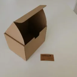 Otwarty, tekturowy pojemnik z delikatnie ząbkowanym brzegiem, obok wizytówka firmy Karton Plus na jasnym tle.