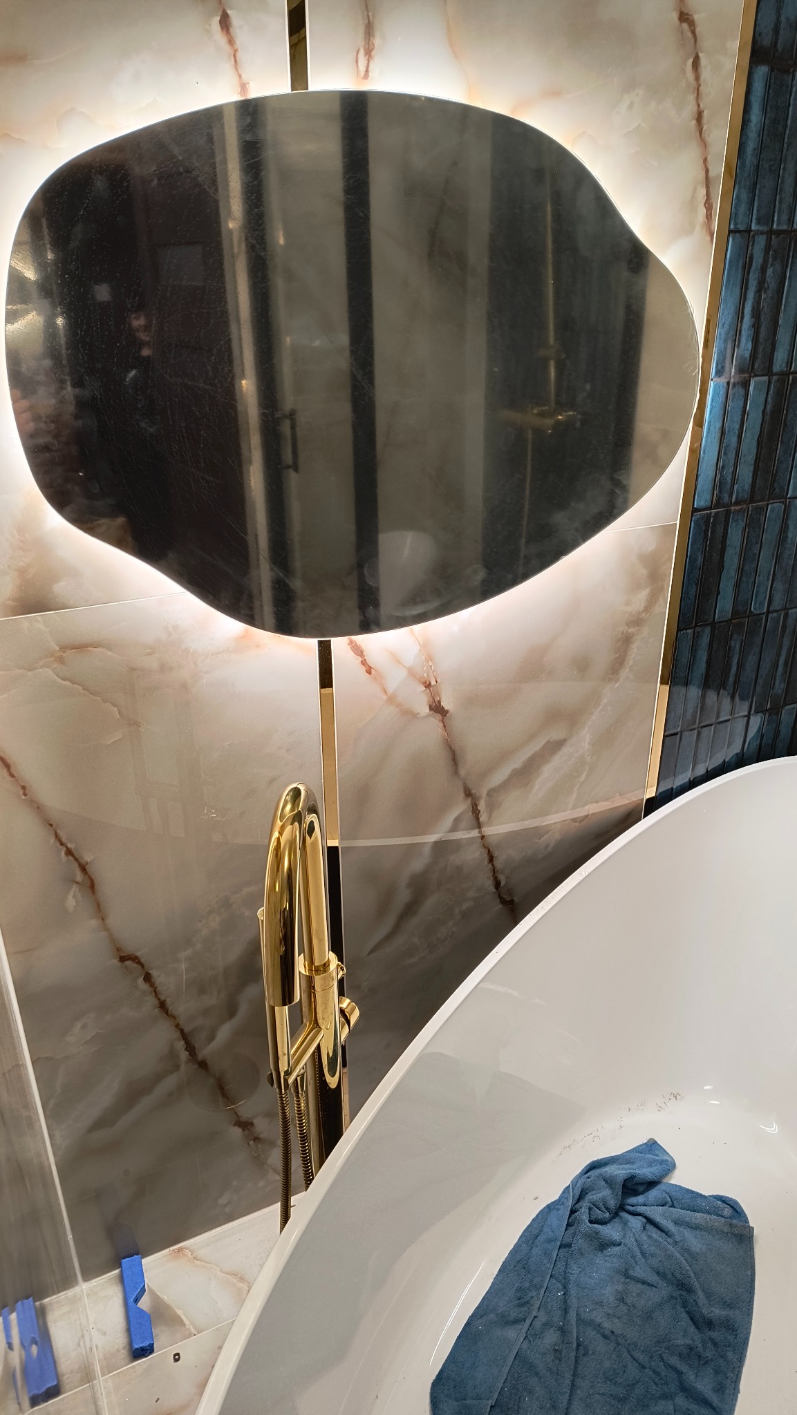 Nowoczesna łazienka: biała wanna, złota armatura i lustro z podświetleniem na tle marmurowych płytek i mozaiki.