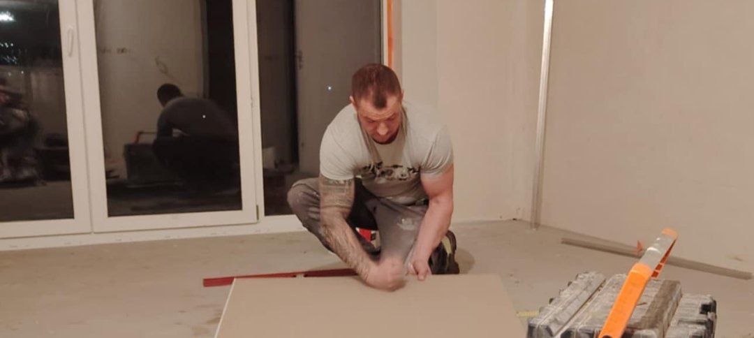 Mężczyzna w trakcie docinania płyty gipsowo-kartonowej w pomieszczeniu z dużym oknem. Widoczne narzędzia i fragment ściany w trakcie prac wykończeniowych.