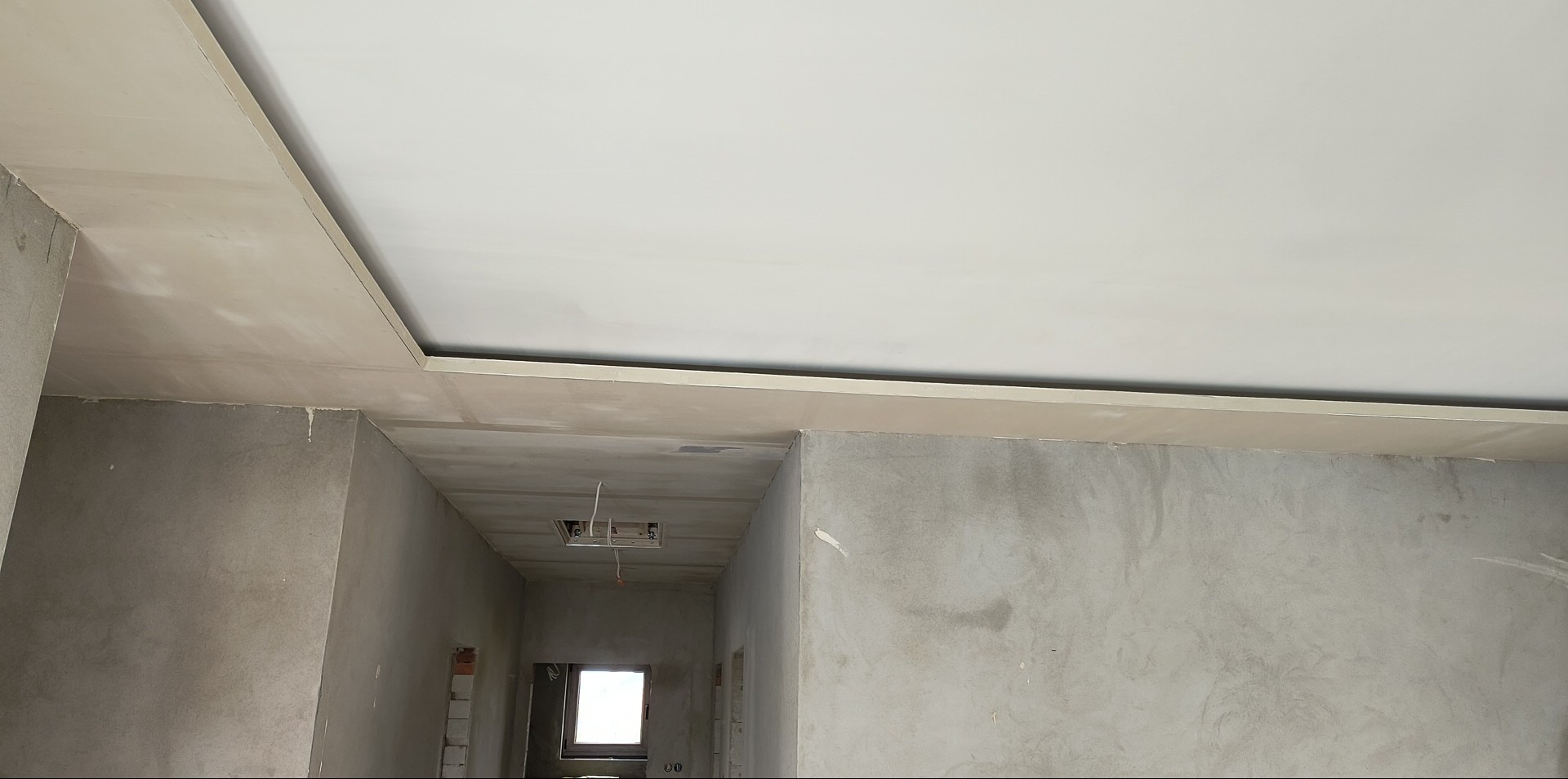 Sufit podwieszany z płyt karton-gips na metalowej konstrukcji, widok z dołu. Szpachlowane ściany w surowym stanie, przygotowane do malowania. Widoczne kable elektryczne.