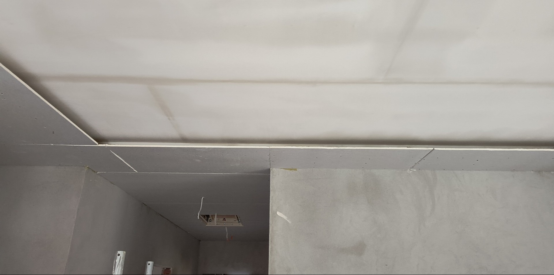 Montaż sufitu z płyt gipsowo-kartonowych w trakcie prac wykończeniowych. Widoczne łączenia płyt i otwór na instalację elektryczną. Szpachlowane ściany w tle.