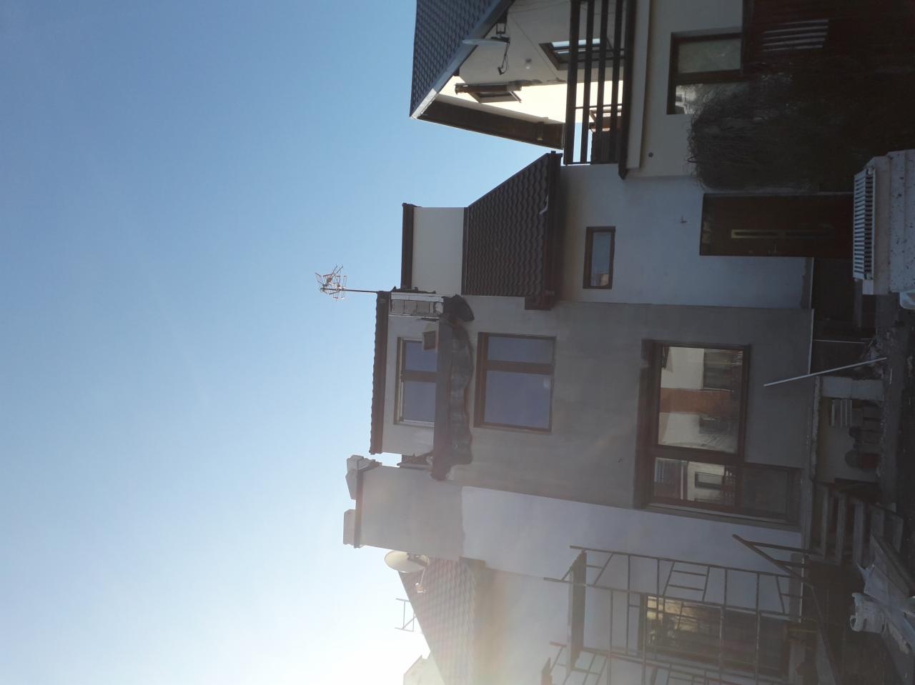 Dom jednorodzinny w trakcie prac remontowych elewacji, z widocznym rusztowaniem i nowym pokryciem dachowym z brązowej dachówki, antena telewizyjna na szczycie budynku.