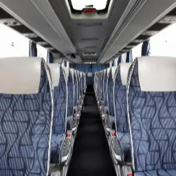 Wnętrze autobusu z rzędami niebieskich foteli z geometrycznym wzorem i białymi zagłówkami, widok z perspektywy pasażera.