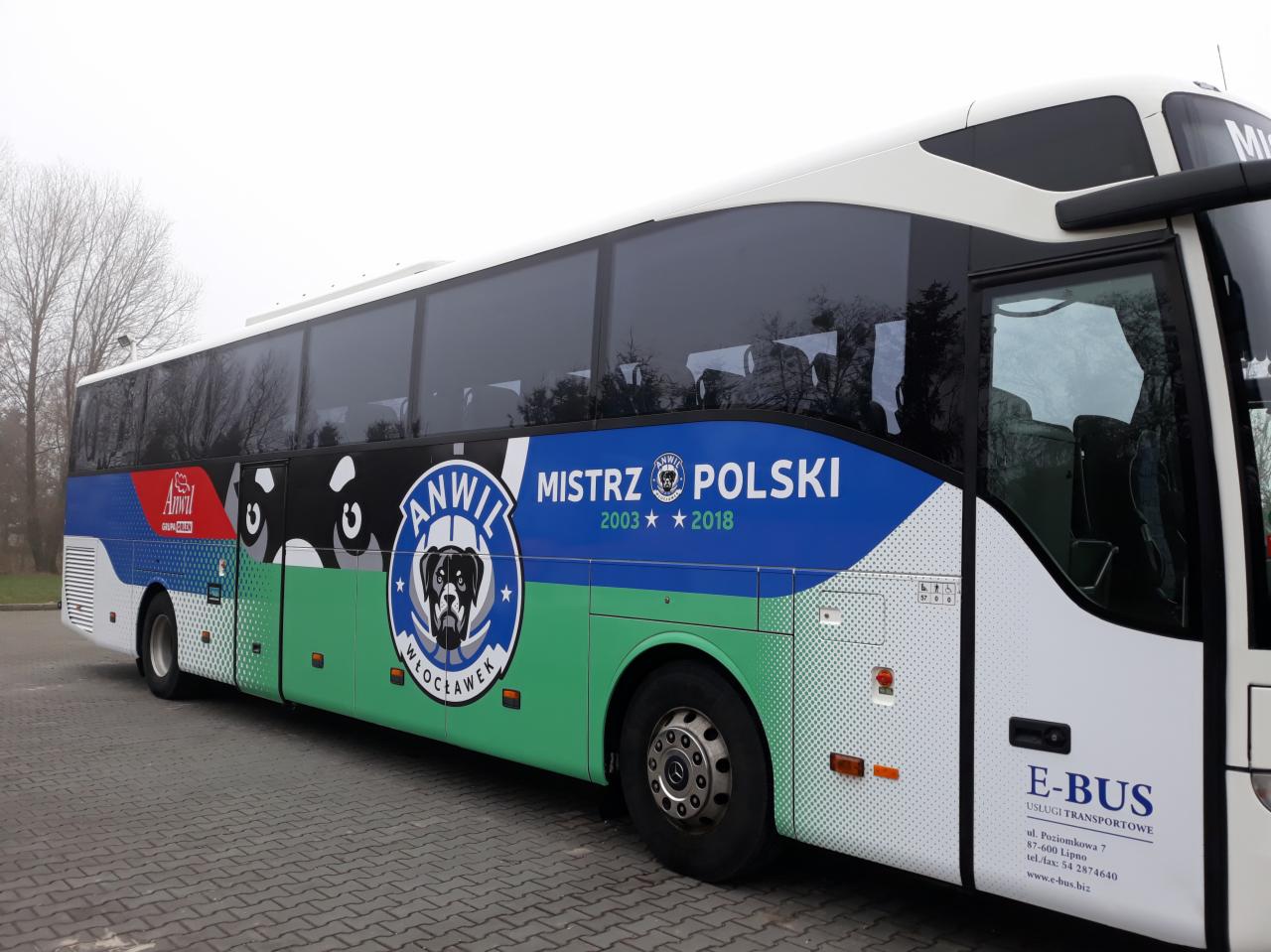 Autokar z reklamą drużyny sportowej Anwil Włocławek, mistrza Polski z lat 2003 i 2018, zaparkowany na brukowanym placu.