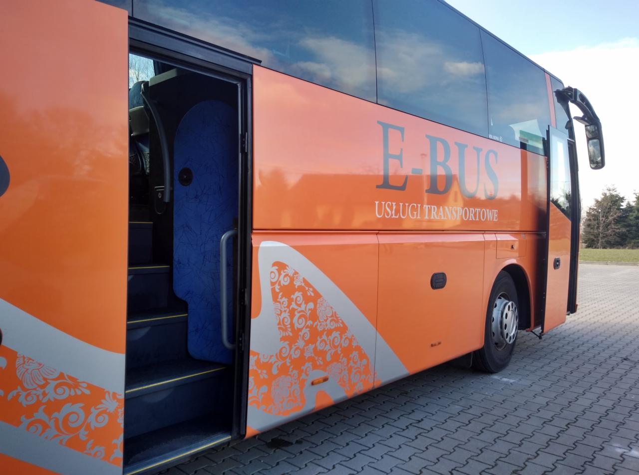 Pomarańczowy autobus z otwartymi drzwiami, widoczne niebieskie obicie wewnątrz i ozdobne wzory na karoserii.