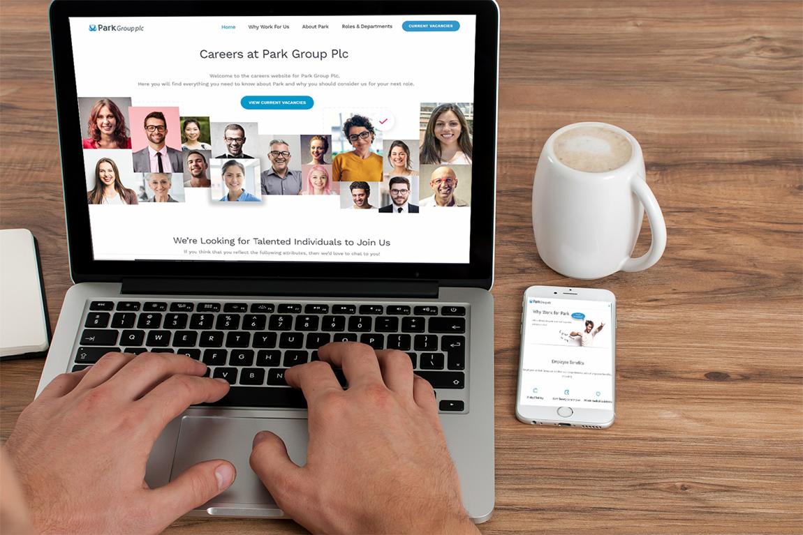 Osoba pisze na laptopie z otwartą stroną kariery Park Group Plc; obok stoi smartfon z wyświetloną wersją mobilną strony i biały kubek z kawą na drewnianym biurku.