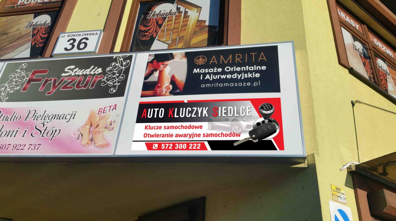 Zewnętrzny szyld reklamowy z ofertą usług: dorabianie kluczy samochodowych i awaryjne otwieranie aut, umieszczony nad salonem fryzjerskim i gabinetem masażu.