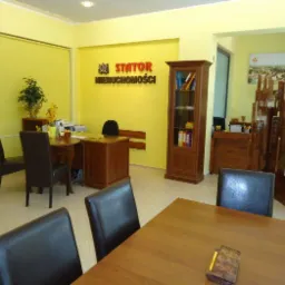 Jasne biuro agencji nieruchomości z drewnianymi meblami, logo firmy na ścianie i dekoracyjnym parawanem z motywem miejskim.