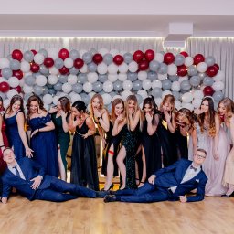 Leszek Dopke Fotografia - Grupa elegancko ubranych kobiet i dwóch mężczyzn w garniturach pozuje na tle ściany z balonów w Orle, z zaskoczonymi minami i rozbawieniem.