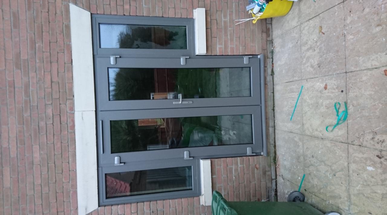 Szare okno z trzema szybami zamontowane w ceglanym murze w Newcastle under Lyme, widoczne ślady po montażu na chodniku.