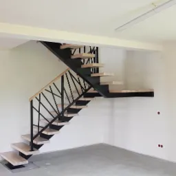 Nowoczesne schody metalowe z drewnianymi stopniami i geometryczną balustradą w surowym, jasnym wnętrzu w trakcie wykończenia.