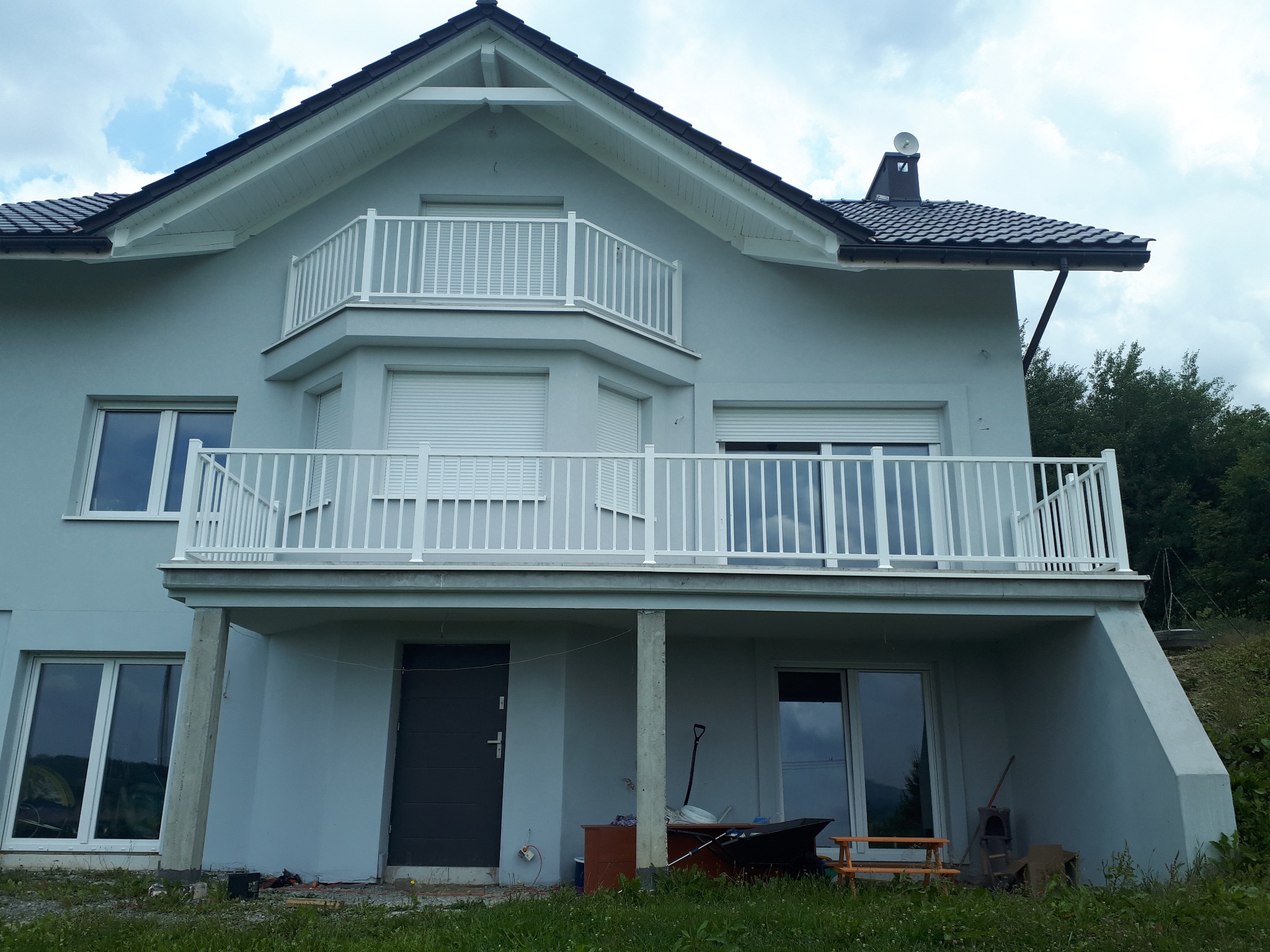 Szary dom jednorodzinny z białymi balustradami balkonowymi na dwóch poziomach, widok z dołu, z elementami wyposażenia na poziomie gruntu.