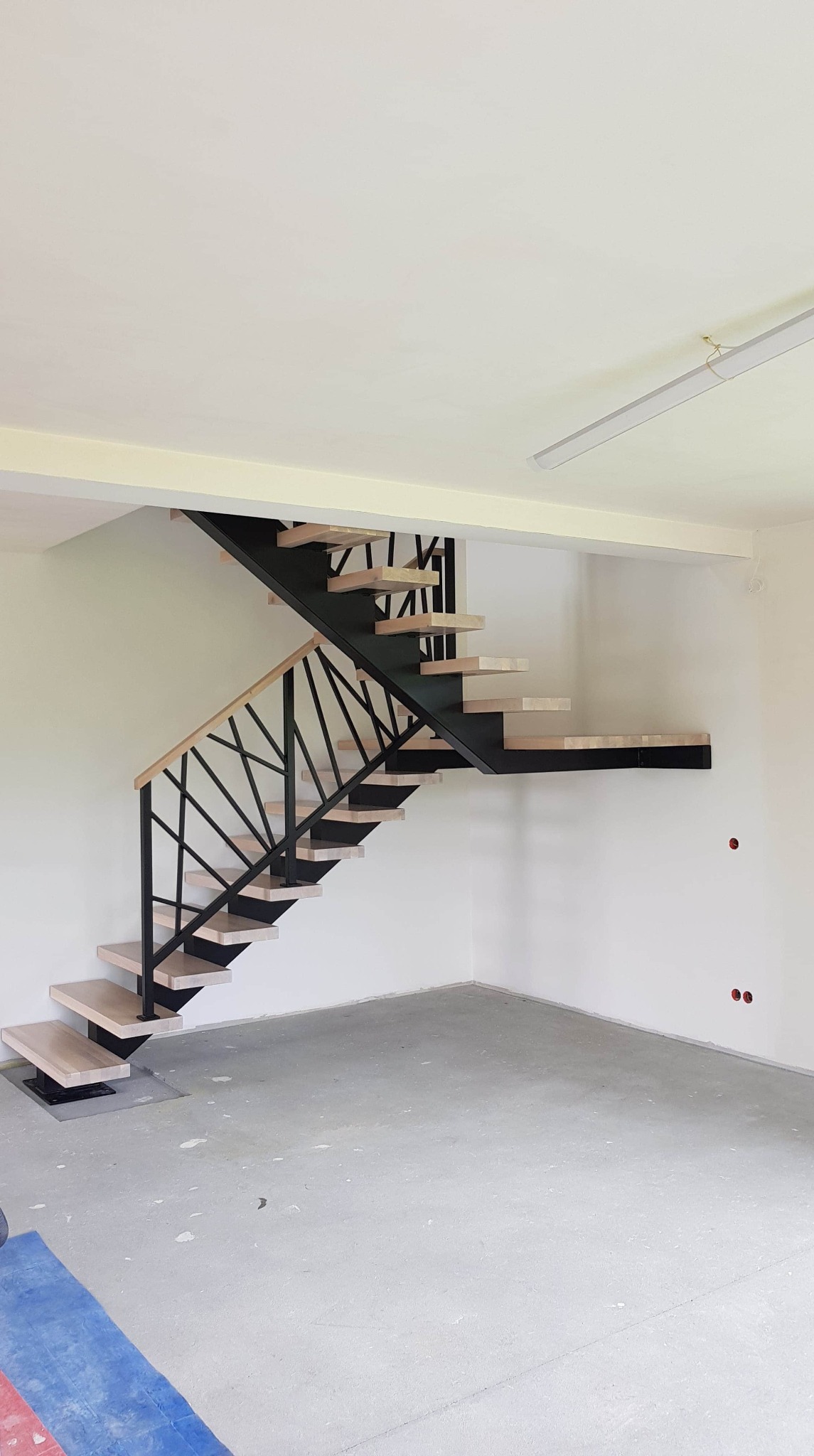 Nowoczesne schody metalowe z drewnianymi stopniami i geometryczną balustradą w surowym, jasnym wnętrzu w trakcie wykończenia.