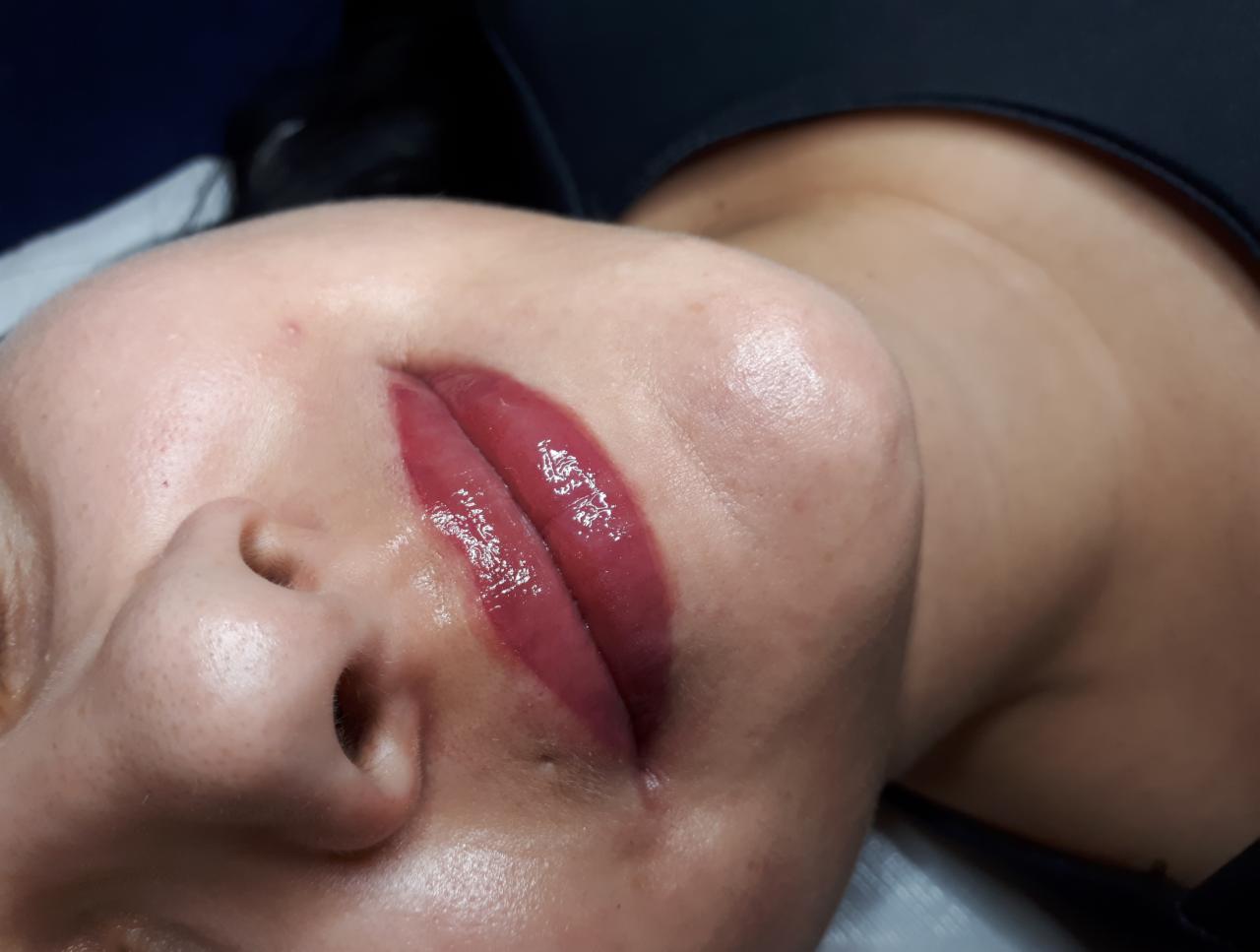 Zbliżenie na usta kobiety po zabiegu makijażu permanentnego, widoczne świeże pigmentacja i połysk.