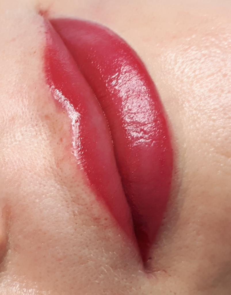 Zbliżenie na usta z makijażem permanentnym, intensywny odcień czerwieni, widoczne pory skóry wokół ust.