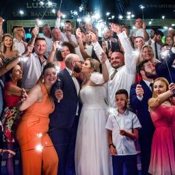 arturgeorgiew - Pocałunek młodej pary otoczonej gośćmi weselnymi z zimnymi ogniami na tle sali bankietowej Luxor.