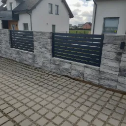 Nowoczesne ogrodzenie z betonowych bloczków o marmurkowym wzorze i poziomych, grafitowych przęsłach, widok z poziomu kostki brukowej.