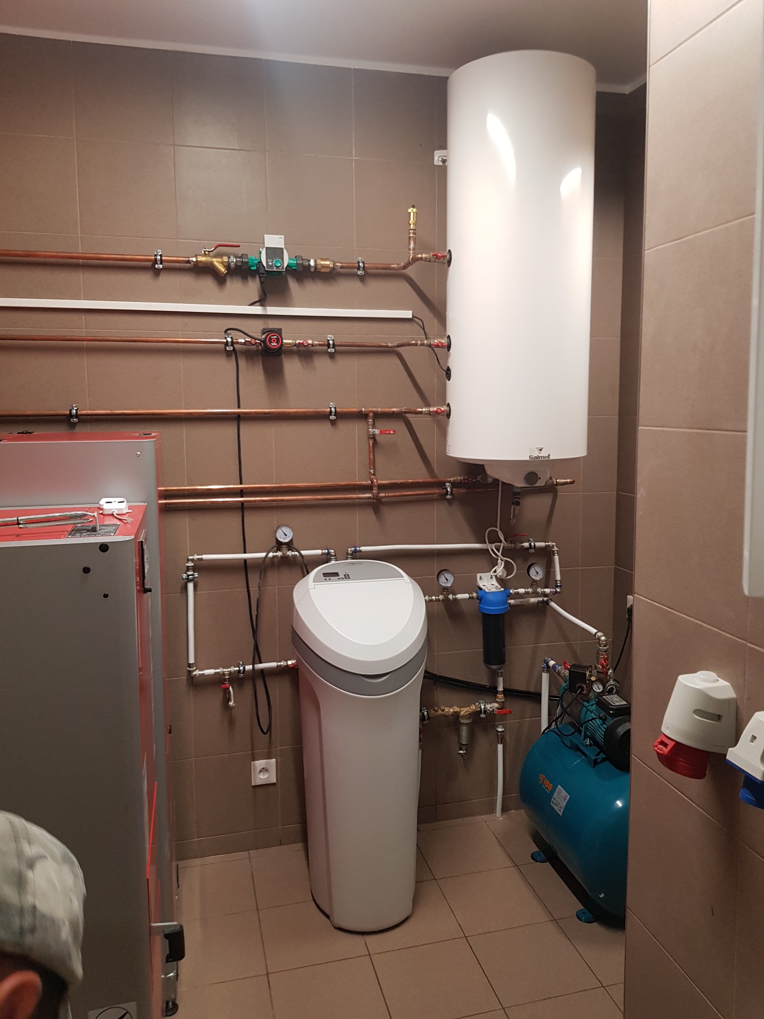 W kotłowni zainstalowano pionowy, biały bojler Galmet, zmiękczacz wody, hydrofor w kolorze turkusowym i piec centralnego ogrzewania z licznymi rurami miedzianymi i plastikowymi.