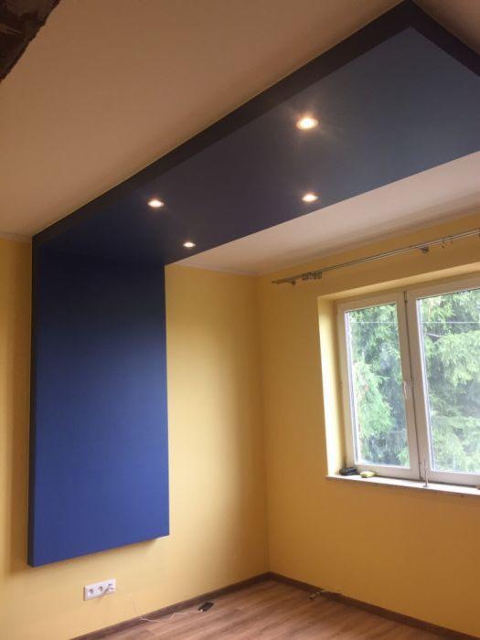 Żółta ściana pokoju z niebieskim panelem ściennym i podwieszanym sufitem z oświetleniem punktowym, widok na okno.